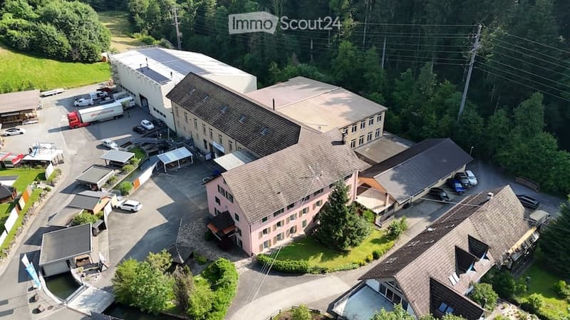 Aerial view of a multi-building industrial or commercial complex with parking areas, surrounded by greenery.