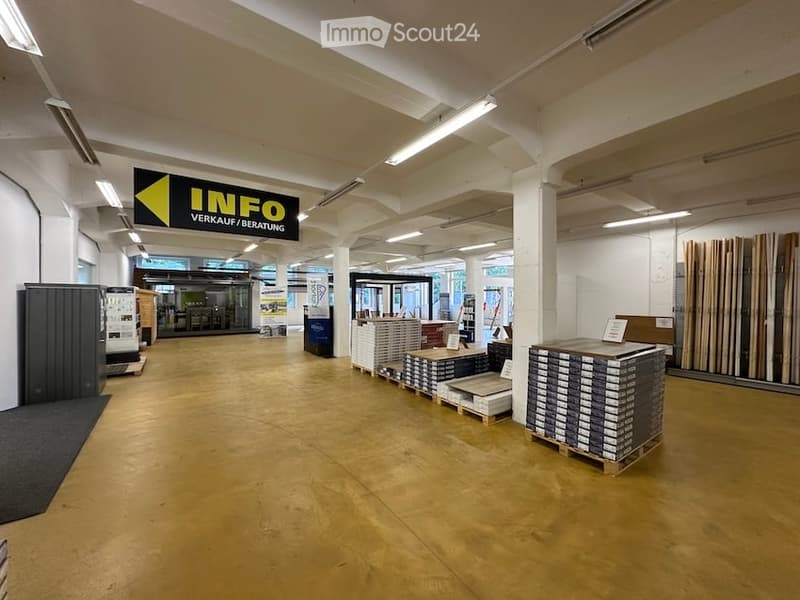 Empty warehouse or showroom space with wooden flooring, white walls, and industrial lighting. No furniture or equipment present.