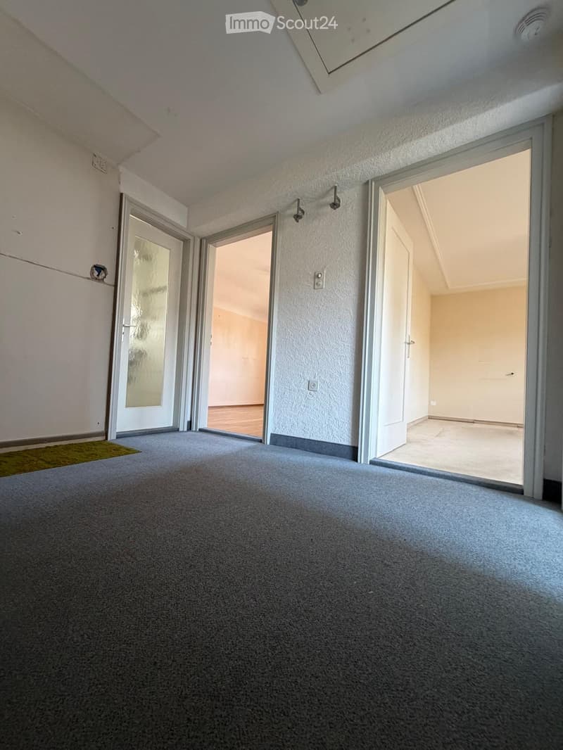 Empty room with grey carpet, white walls, and multiple open doors leading to other spaces.