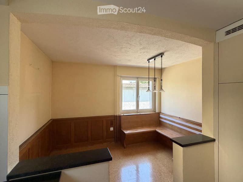 Empty room with beige walls, wooden paneling, built-in benches, and a window with a view of the outside.