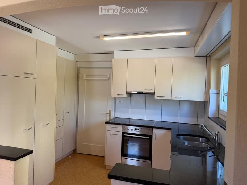 Modern kitchen with white cabinets, stainless steel oven, black countertops, and a window.