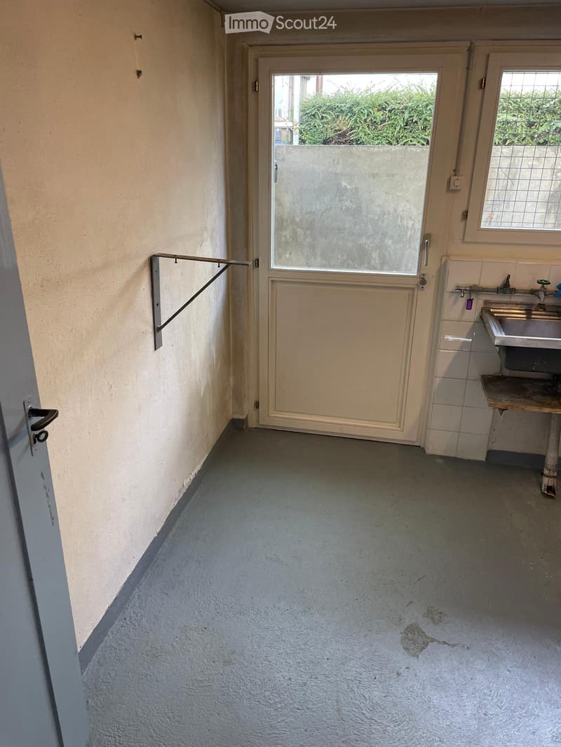 Empty hallway with a door leading to an outdoor area, a sink, and a window with bars.