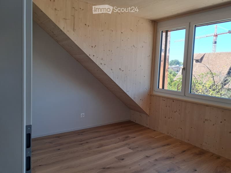 Empty room with wooden walls and floor, large windows, and visible electrical outlet.