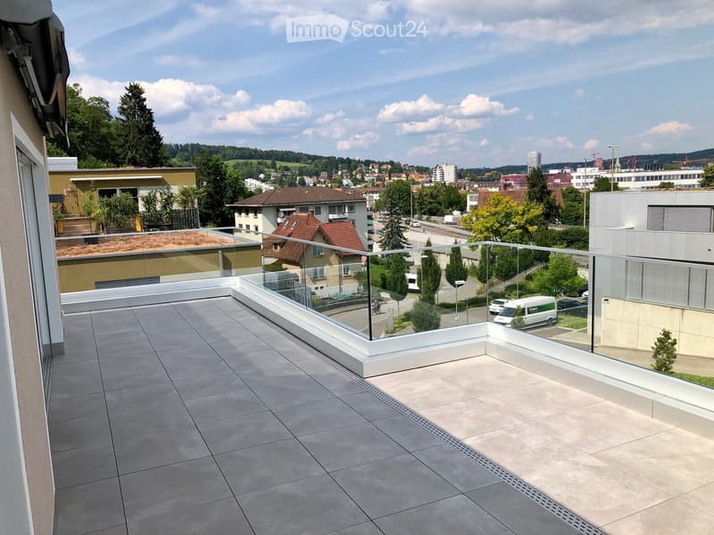 Modern balcony with tiled floor, glass railing, and scenic city view.