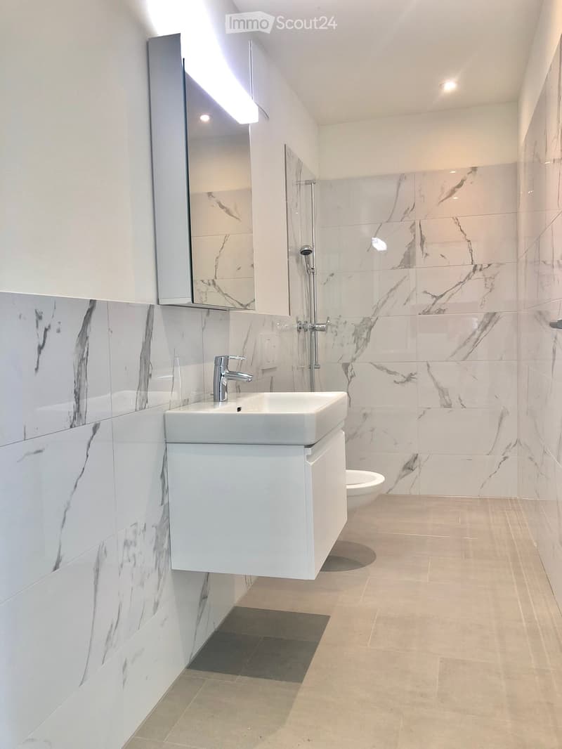 Modern bathroom with white marble tiles, a white sink with a modern faucet, a mirrored cabinet, and a glass-enclosed shower area.