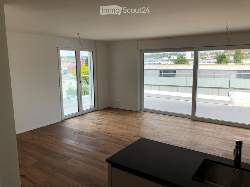 Empty room with wooden flooring, large sliding glass doors leading to a balcony, and a small black countertop with a sink and faucet.