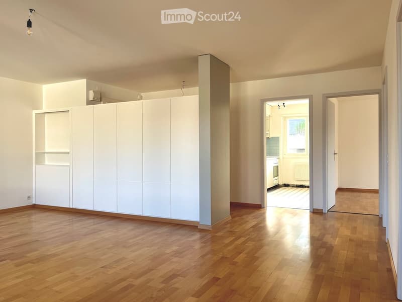 Empty room with wooden flooring, white walls, built-in white closet, and open doorways leading to other rooms.