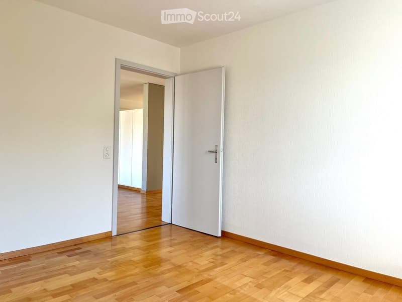 Empty room with light-colored walls and wooden flooring, featuring an open doorway leading to another room.