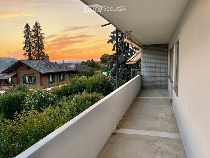 Balcony with a view of a garden and a house in the background during sunset.