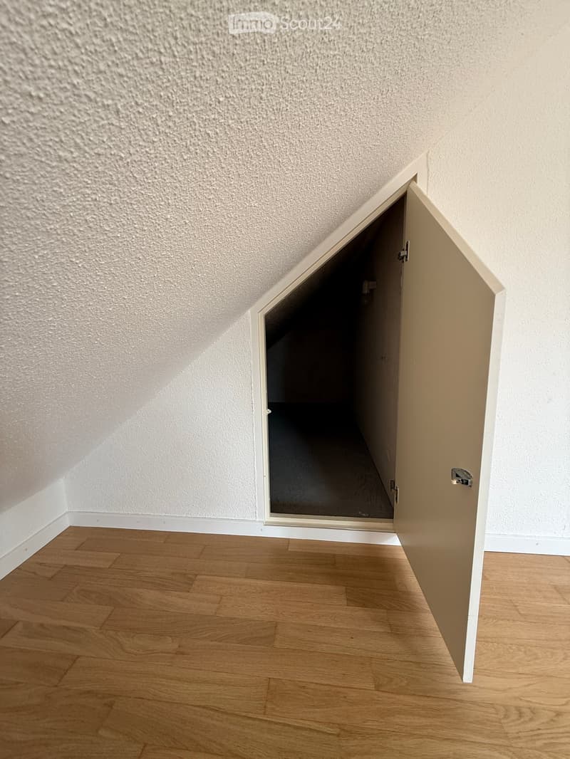 Empty room with wooden flooring and white walls, featuring an open door leading to another space.