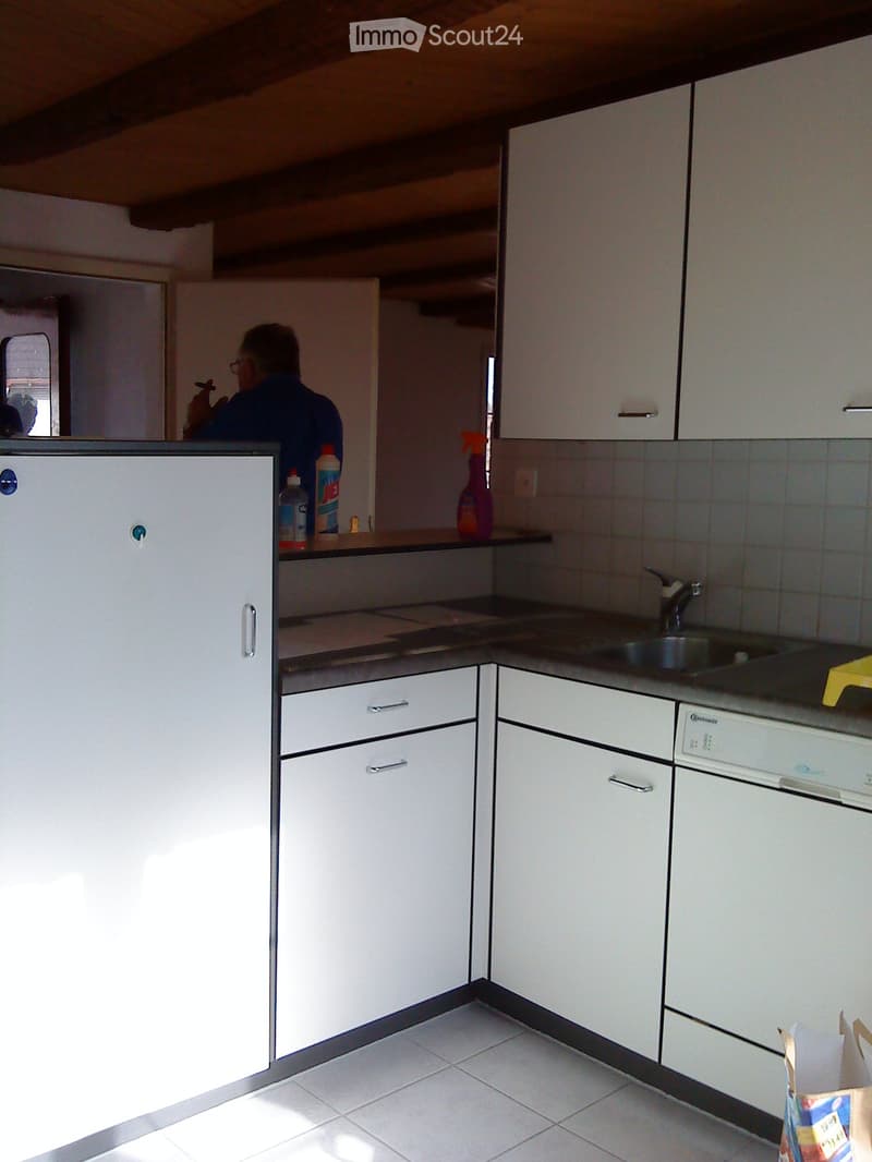 modern kitchen with white tiles, cabinets, countertop, sink, dishwasher, bottles, yellow sponge, wooden beam