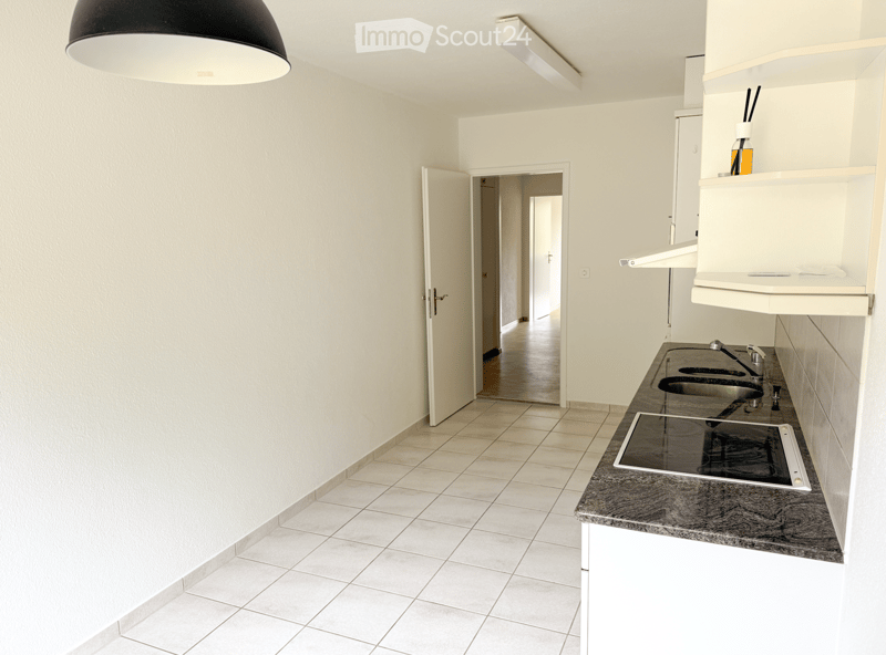 Modern kitchen with white cabinets, granite countertop, electric stove, double sink, and shelves. The space is clean and well-lit with tiled flooring.