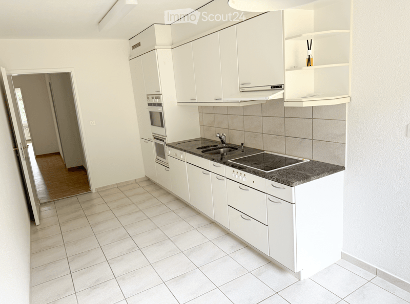 Modern kitchen with white cabinets, granite countertop, stainless steel sink, electric stove, and built-in oven. Light-colored tiled floor and walls.