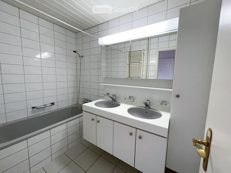Modern bathroom with white tiles, double sink, bathtub, large mirror, and built-in cabinets.