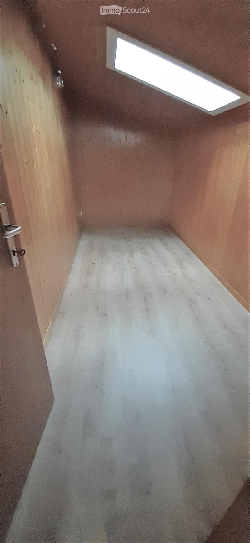 Empty room with wooden walls, concrete floor, and a small window at the top.