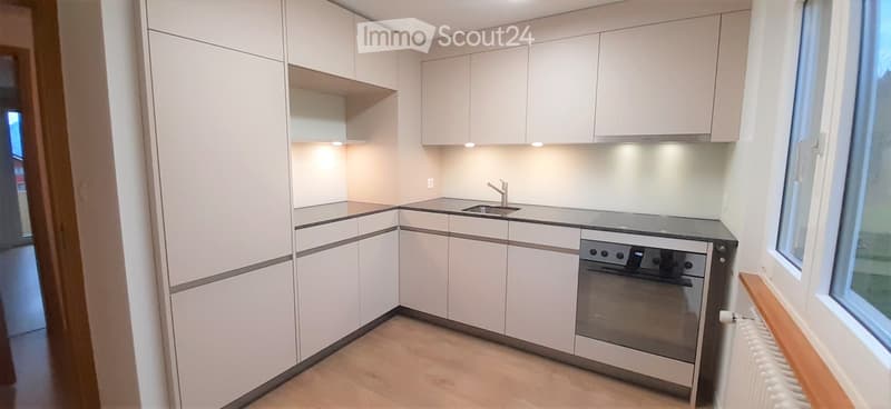 Modern kitchen with white cabinets, a sink, and an oven, featuring a light wooden floor and built-in lighting.