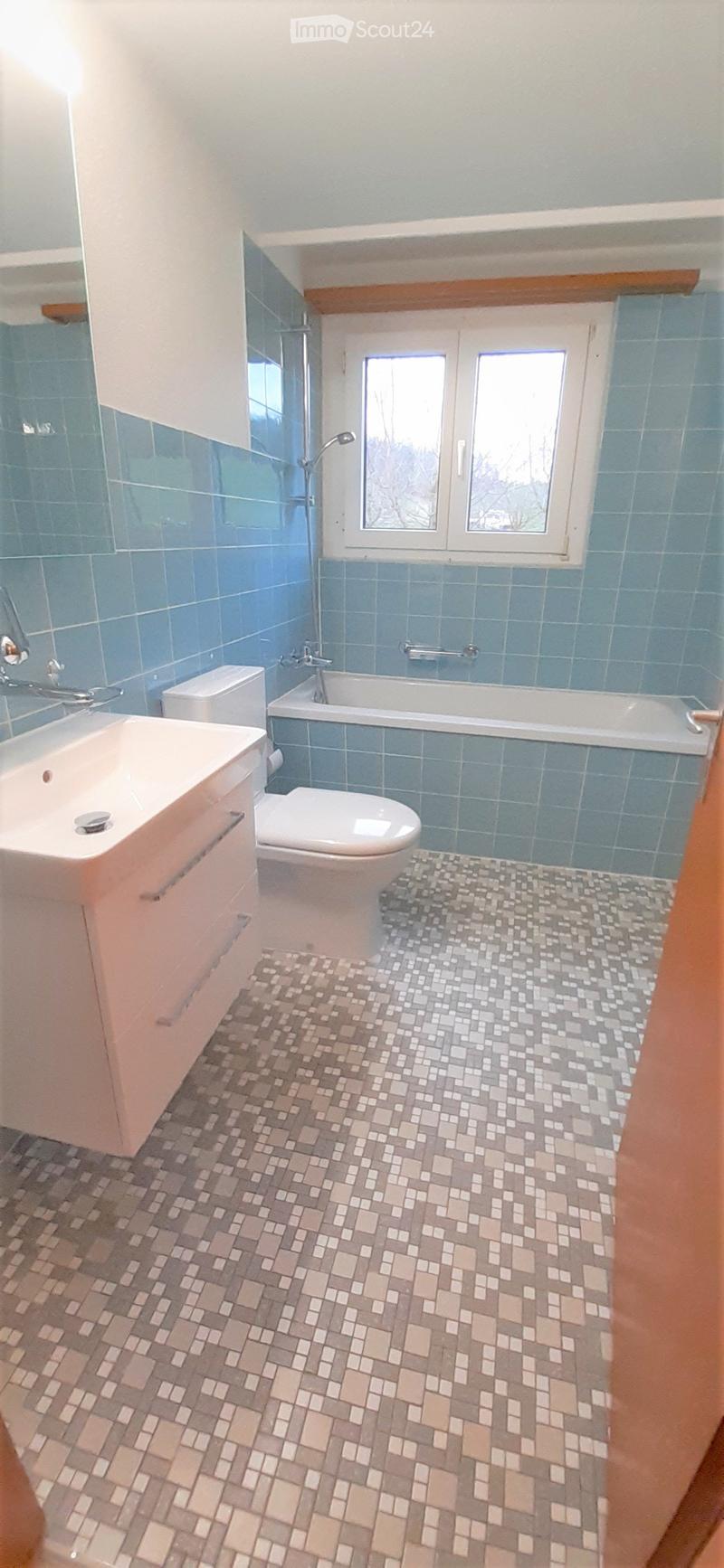 Bathroom with blue tiled walls, a white sink, toilet, bathtub, and a window with two panes.