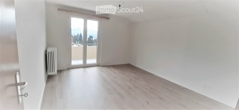 Empty room with light wooden flooring, white walls, and a large glass door leading to a balcony with a scenic mountain view.
