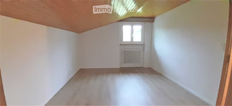 Empty room with white walls, wooden ceiling, and a single window with a radiator below it.
