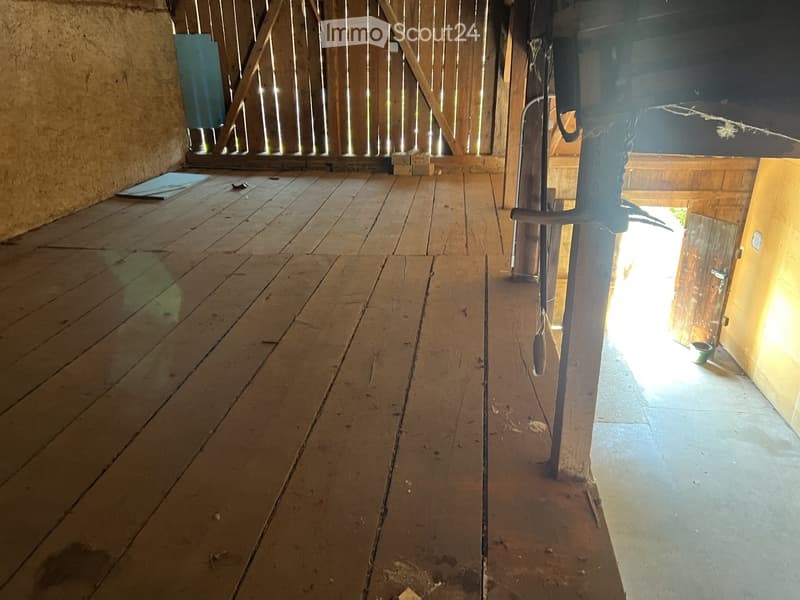 Empty wooden room with exposed beams, wooden floor, and a small opening to another area.
