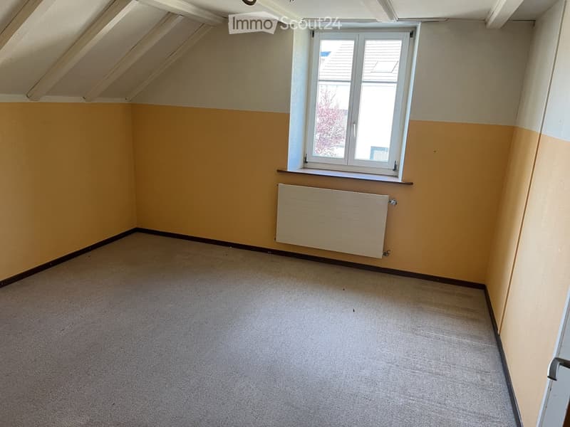 Empty room with beige walls, carpeted floor, and a single window with a radiator below it.