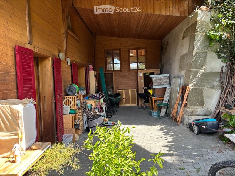 Outdoor storage area with wooden walls, stone pillar, and various stored items including crates, tools, and a lawnmower.