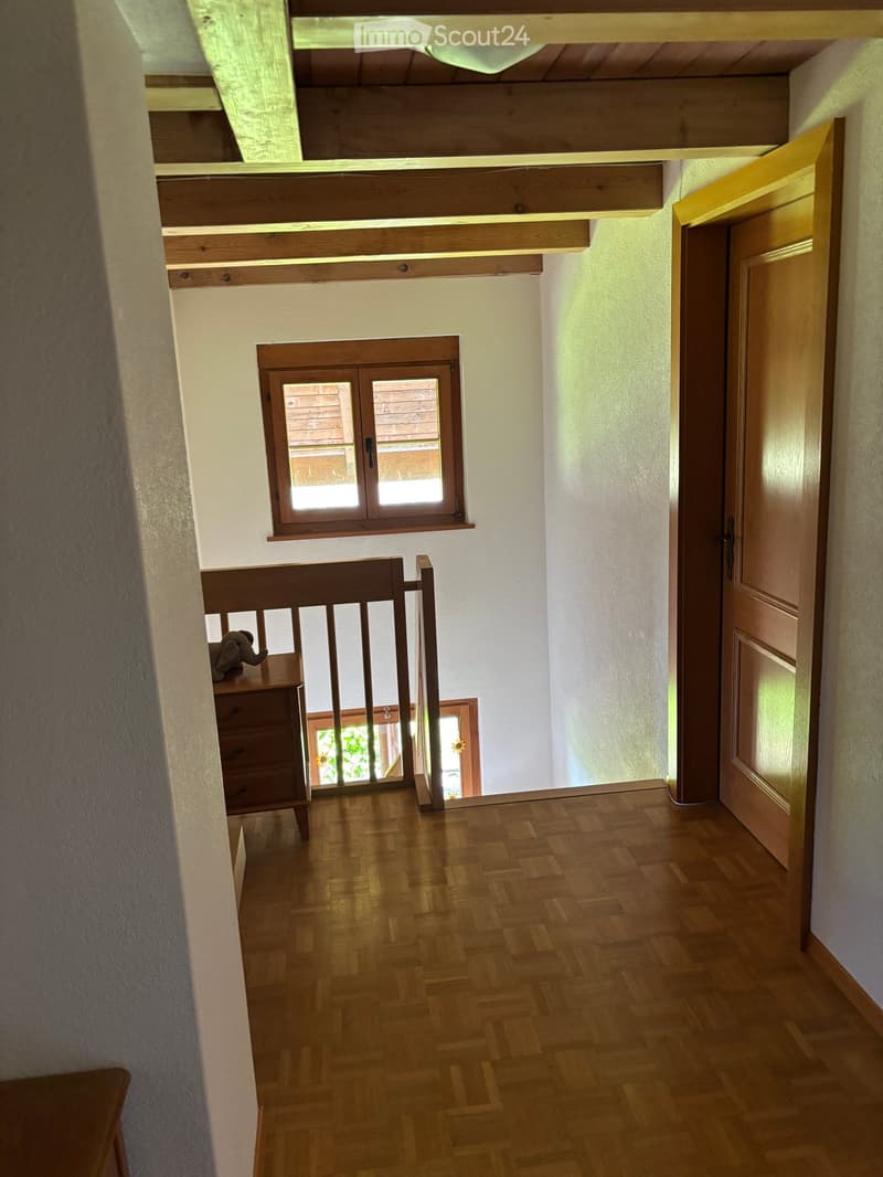 Wooden hallway with a staircase, wooden railing, and a small window. A small wooden cabinet with drawers is visible on the left side.