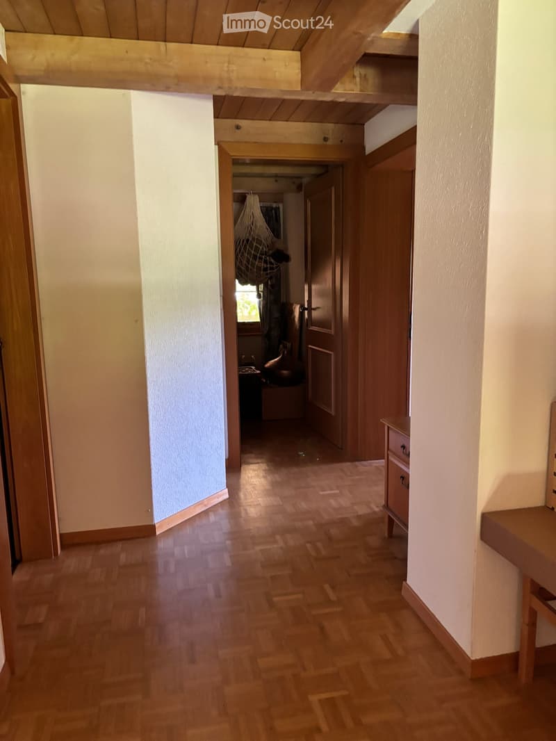 Wooden-floored hallway with white walls, wooden doors, and a small bench on the right side.