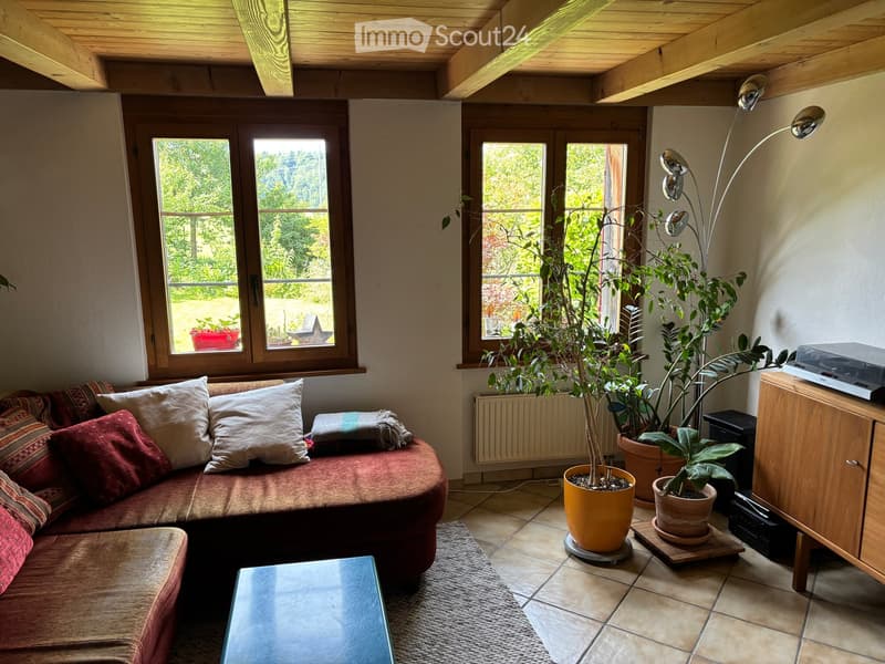 Cozy living room with a red sofa, white pillows, a coffee table, potted plants, and a floor lamp near the windows.