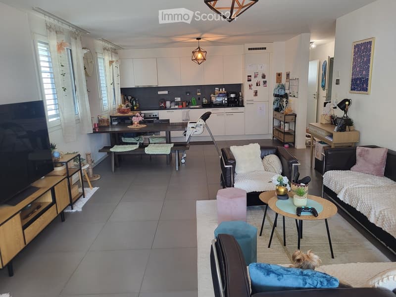 Open-plan living and dining area with modern furniture, including a sofa, coffee table, dining table, and kitchen area with cabinets and appliances.