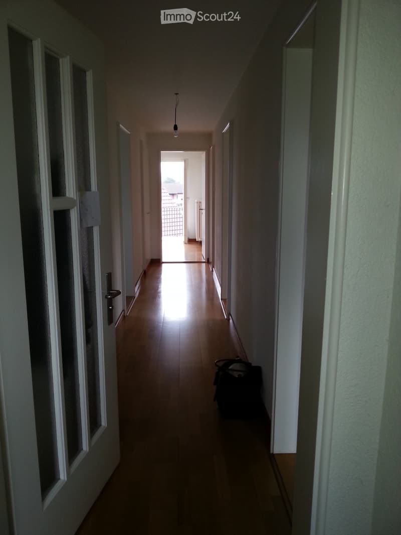 Empty corridor, white walls, wooden floor, closed doors, open hallway with window.