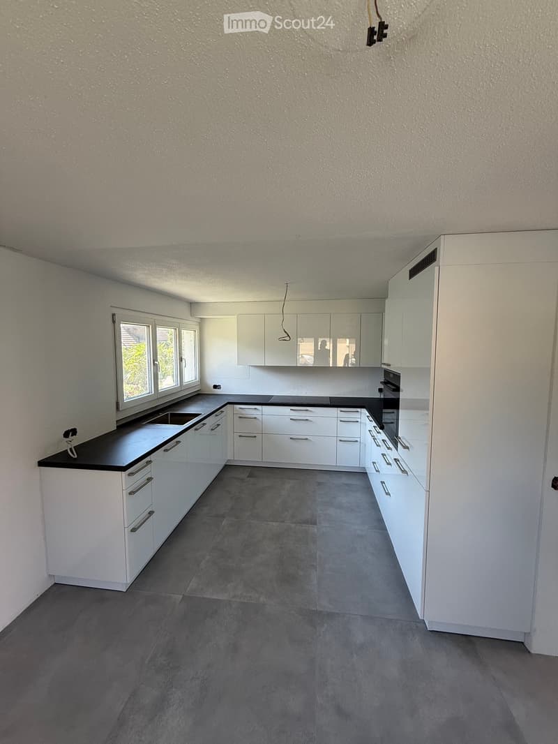 Empty kitchen with white cabinets, black countertops, and grey tiled floor. No appliances or furniture present.