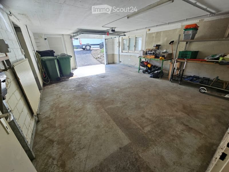 Garage with concrete floor, shelves, tools, storage bins, radiator, and trash bins.