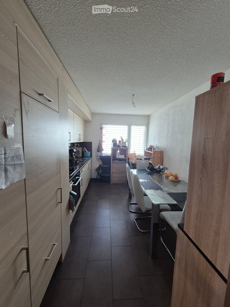 Modern kitchen with wooden cabinets, dark tiled floor, and a glass dining table with chairs.