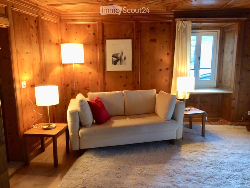 Cozy living room with wooden walls, a light-colored sofa with red throw pillows, two side tables with lamps, and a large picture frame on the wall.