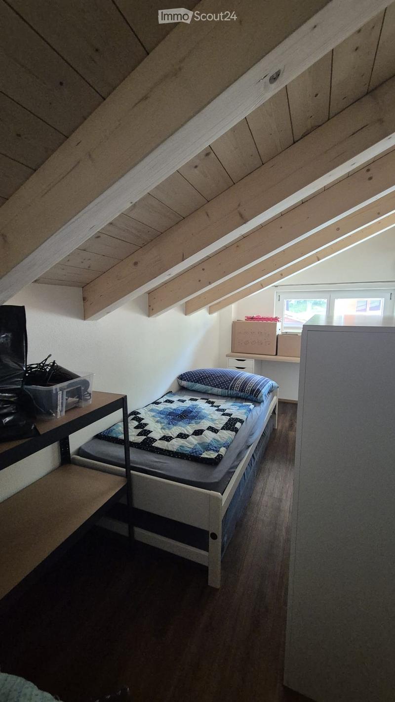 Cozy attic bedroom with wooden slanted ceilings, a single bed with a blue and white quilt, a small table, and storage boxes.