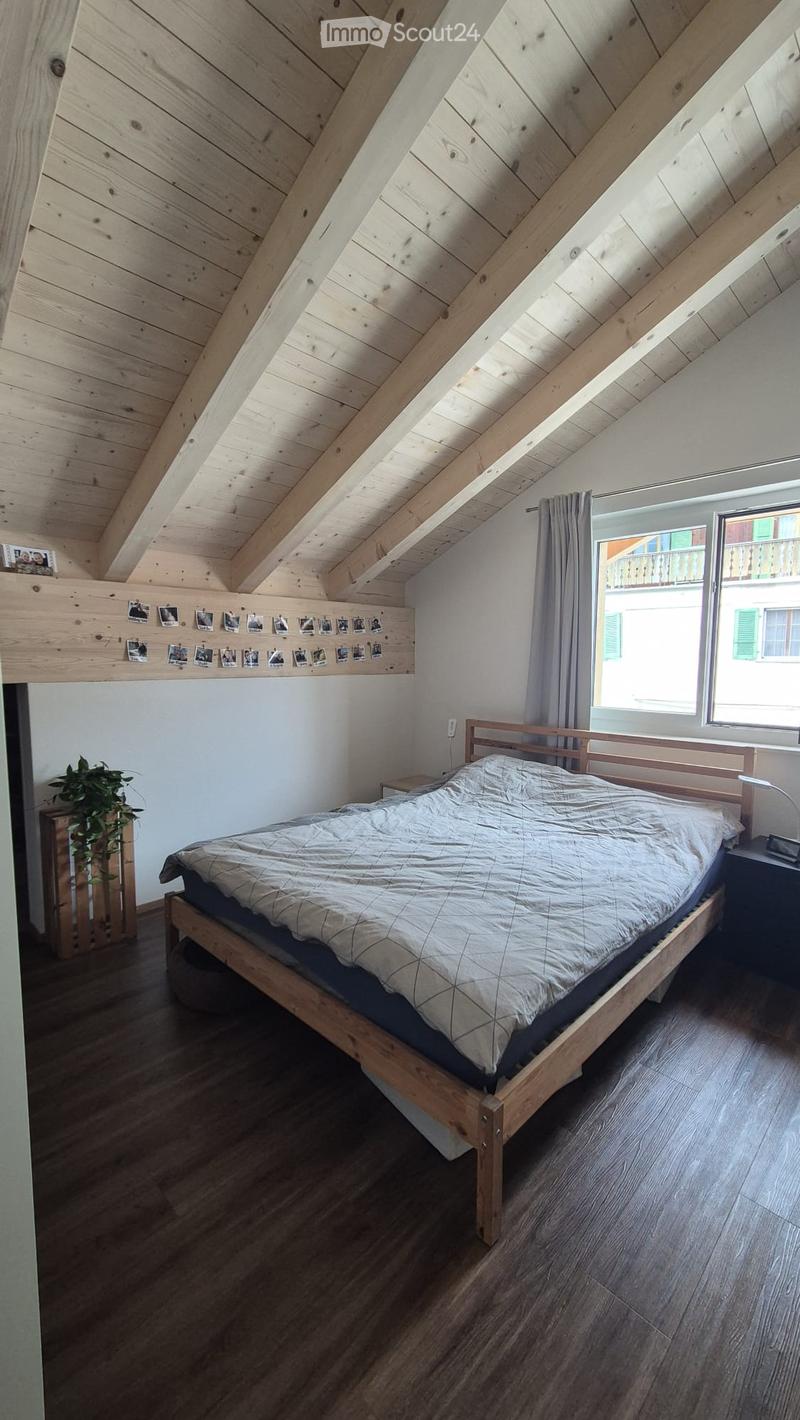 Cozy attic bedroom with wooden slanted ceilings, a wooden bed, nightstand, and a small plant near the window.