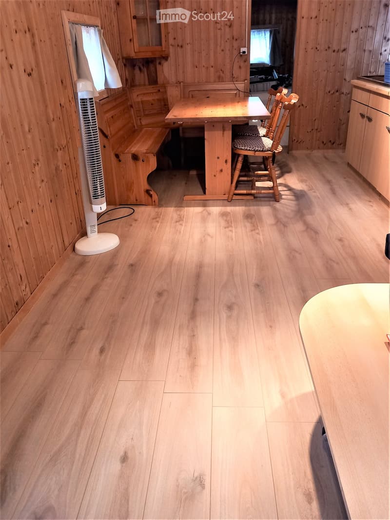 Cozy wooden interior with a dining table, chairs, and a fan. Light wooden flooring and walls.