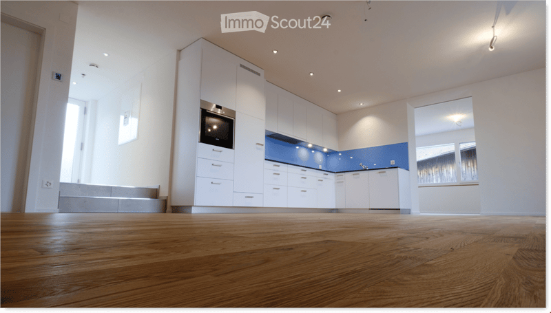 Empty kitchen with white cabinets, wooden floor, and blue backsplash. No furniture or appliances visible.