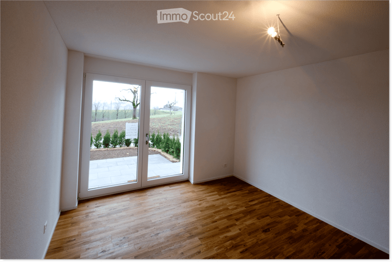 Empty room with wooden flooring, white walls, and large sliding glass doors leading to an outdoor area.