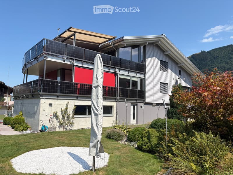 Modern two-story house with large windows, balconies, solar panels, and a well-maintained garden.