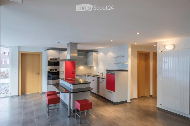 Modern kitchen with white cabinets, stainless steel appliances, a central island with a black countertop, and red stools.