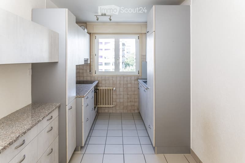 Modern kitchen with white cabinets, granite countertop, tiled floor, and a window overlooking a building.
