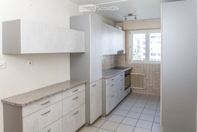 Modern kitchen with light grey cabinets, granite countertop, tiled floor, and a radiator under the window.