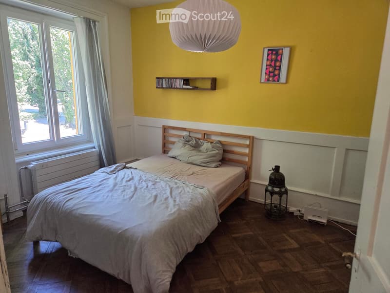 Bright bedroom with yellow walls, wooden bed, shelves, and a large window with curtains.
