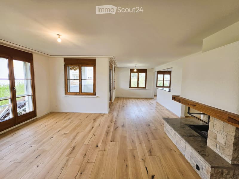 Empty room with hardwood floors, white walls, large windows, and a fireplace with a stone mantle.