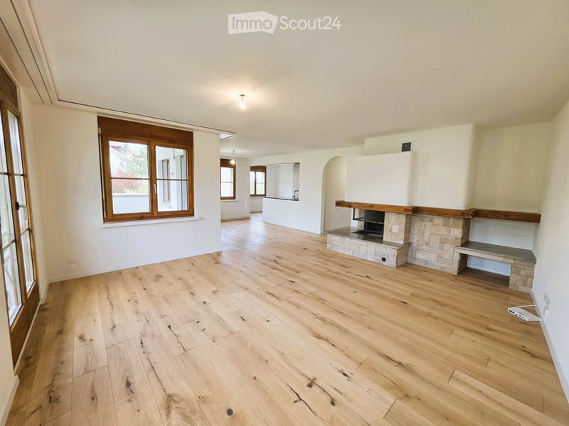 Empty room with hardwood floors, white walls, and large windows. A fireplace is built into the wall.