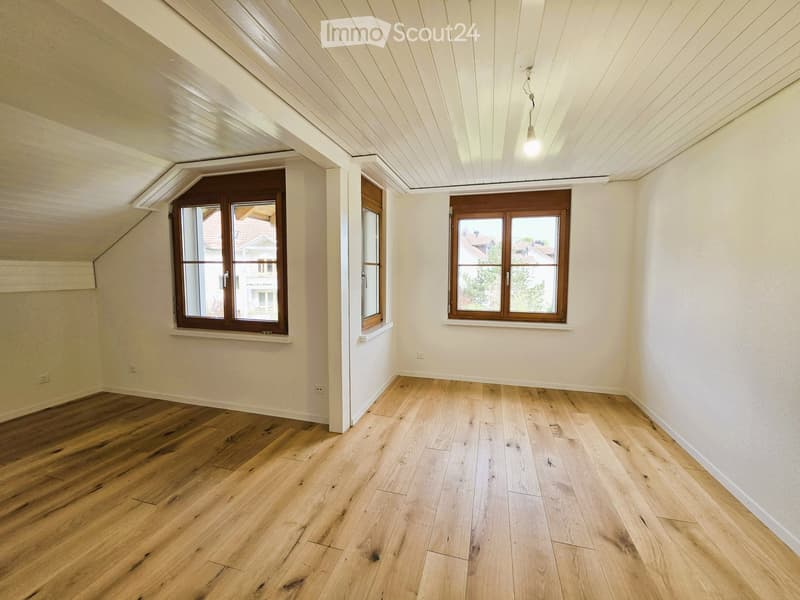 Empty room with wooden floors, white walls, and two windows with wooden frames. There are no visible objects in the room.