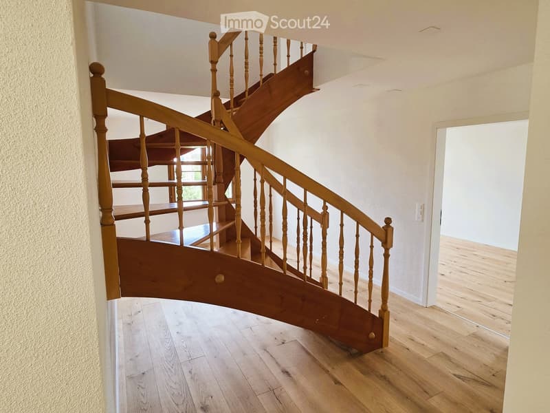 A wooden spiral staircase with a white wall on the left and a white door on the right.