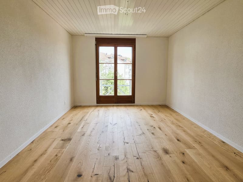 Empty room with wooden floors, white walls, and a wooden door leading to a balcony.